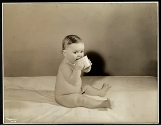Ein Baby sitzt im Bett und trinkt aus einer Tasse im Maternity Center Association an der 70th Street East River, New York, 1935